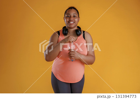 Bottle of water, break, standing with headphones on the neck. African American woman is in the studio Bottle of water, break, standing with headphones on the neck. African American woman is in the studio 131394773