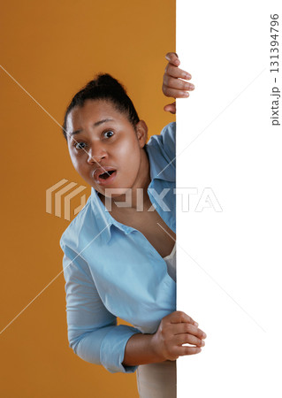 White copy space wall, hiding behind it. African American woman is in the studio against yellow background White copy space wall, hiding behind it. African American woman is in the studio against yellow background 131394796