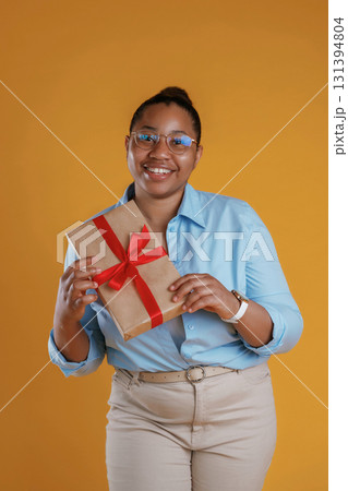 Holidays time, holding gift box. African American woman is in the studio against yellow background 131394804