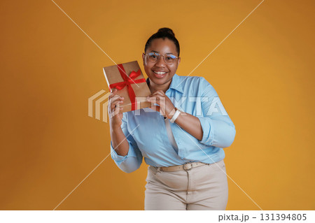 Holidays time, holding gift box. African American woman is in the studio against yellow background Holidays time, holding gift box. African American woman is in the studio against yellow background 131394805