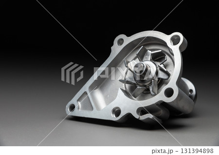 A new, shiny aluminum engine coolant pump on a gray gradient background. Contrast backlighting. A new, shiny aluminum engine coolant pump on a gray gradient background. Contrast backlighting. 131394898
