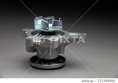 A new, shiny aluminum engine coolant pump on a gray gradient background. Contrast backlighting. 131394908