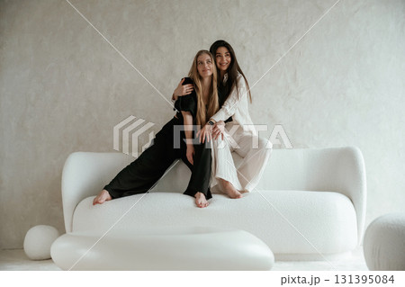 Hugs, on the white sofa. Two happy young female best friends are indoors 131395084