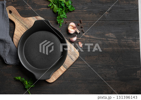 Empty black cast iron pan with herbs and garlic on wooden background 131396143