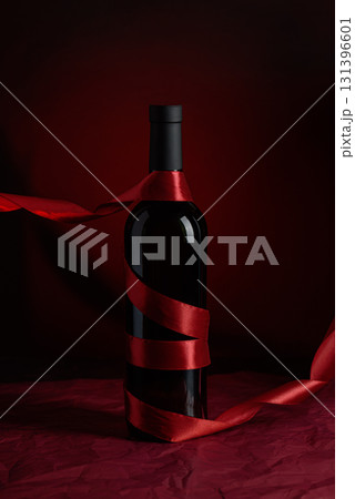 Wine Bottle with Red Satin Ribbon on Dramatic Red Background 131396601