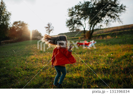 Little girl holding ribbon headband walking in autumn meadow at sunset. 131396834