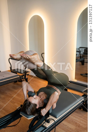 Woman doing Pilates exercise for core and back muscles on Reformer machine with determination and focus on strength body Woman doing Pilates exercise for core and back muscles on Reformer machine with determination and focus on strength body 131397117