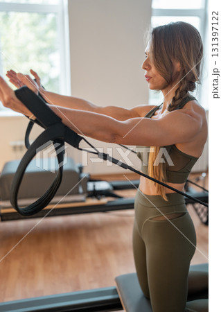 Woman doing pilates exercise on Pilates Reformer for the chest and back muscles, focusing on flexibility, strength, and control with determination Woman doing pilates exercise on Pilates Reformer for the chest and back muscles, focusing on flexibility, strength, and control with determination 131397122