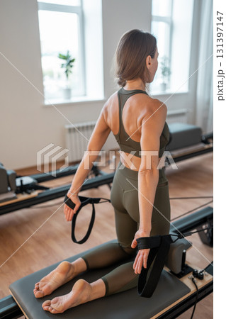 Woman doing pilates exercise on Pilates Reformer for the chest and back muscles, focusing on flexibility, strength, and control with determination 131397147