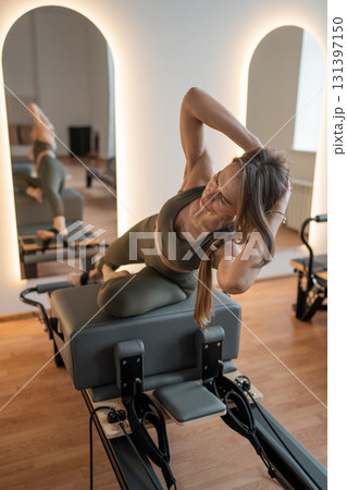 Woman doing Pilates exercise for core and back muscles on Reformer machine with determination and focus on strength body Woman doing Pilates exercise for core and back muscles on Reformer machine with determination and focus on strength body 131397150