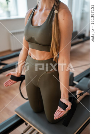Woman doing pilates exercise on Pilates Reformer for the chest and back muscles, focusing on flexibility, strength, and control with determination 131397153