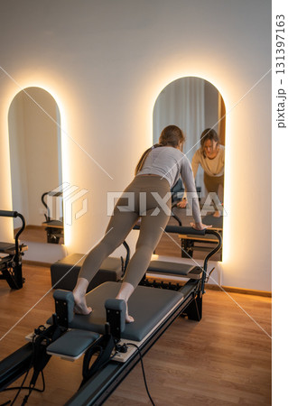 Woman Pilates Instructor Gives Guidance to a men Student While They Utilize the Reformers Equipment 131397163