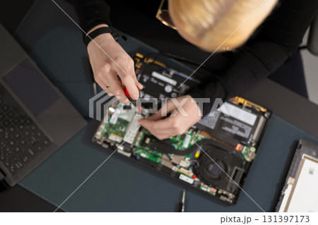 Female IT technician repairs laptop motherboard with screwdriver during maintenance and upgrade session 131397173