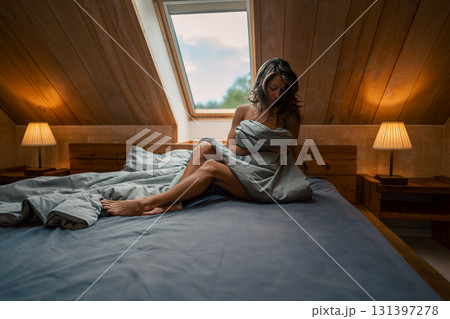 A tranquil scene of a woman wrapped in a cozy blanket, sitting peacefully in a sunlit attic bedroom A tranquil scene of a woman wrapped in a cozy blanket, sitting peacefully in a sunlit attic bedroom 131397278