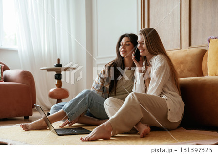 Eavesdrops on what saying on the phone. Two happy young female best friends are indoors 131397325
