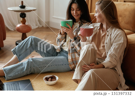 Conversation, with cups of drink. Two happy young female best friends are indoors Conversation, with cups of drink. Two happy young female best friends are indoors 131397332