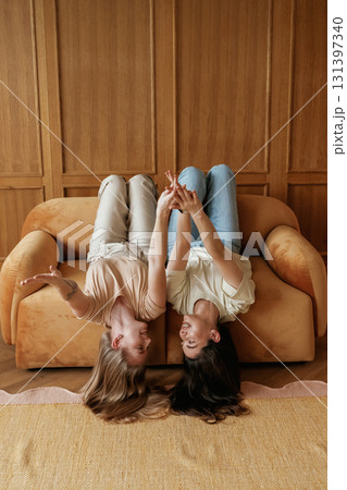Lying upside down on the sofa with heads down. Two happy young female best friends are indoors 131397340