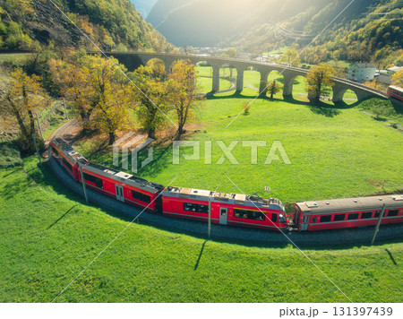 Aerial view of red train on spiral viaduct in mountains at sunset 131397439
