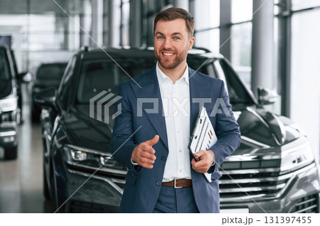 Making a deal, giving a hand, holding notepad. A businessman is in a car dealership Making a deal, giving a hand, holding notepad. A businessman is in a car dealership 131397455
