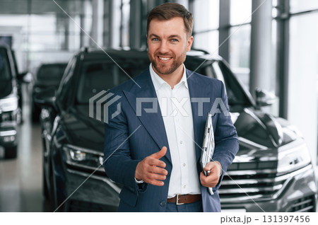 Making a deal, giving a hand, holding notepad. A businessman is in a car dealership Making a deal, giving a hand, holding notepad. A businessman is in a car dealership 131397456