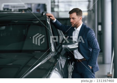 Looking at the automobile. A businessman is in a car dealership Looking at the automobile. A businessman is in a car dealership 131397460