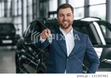 Keys in hand, smiling. A businessman is in a car dealership Keys in hand, smiling. A businessman is in a car dealership 131397461