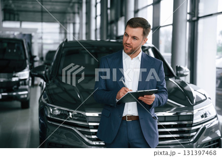 Notepad and pen in hands. A businessman is in a car dealership Notepad and pen in hands. A businessman is in a car dealership 131397468