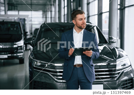 Notepad and pen in hands. A businessman is in a car dealership 131397469