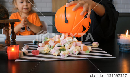 Children excitedly pour colorful candies from a pumpkin shaped basket onto a table in the kitchen celebrating a joyful Halloween party atmosphere filled with treats Children excitedly pour colorful candies from a pumpkin shaped basket onto a table in the kitchen celebrating a joyful Halloween party atmosphere filled with treats 131397537