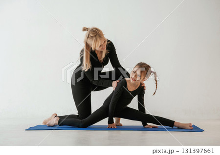 Teaching how to sit on twine. Mother and little daughter are in fitness clothes on yoga mat 131397661