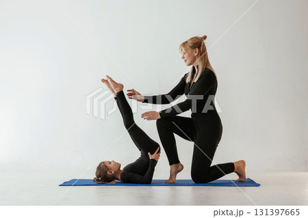 Raising legs up, helping. Mother and little daughter are in fitness clothes on yoga mat Raising legs up, helping. Mother and little daughter are in fitness clothes on yoga mat 131397665