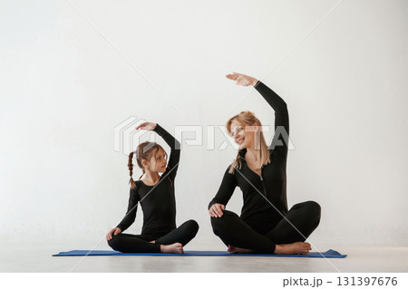 Warm up exercises for hands and spine. Mother and little daughter are in fitness clothes on yoga mat Warm up exercises for hands and spine. Mother and little daughter are in fitness clothes on yoga mat 131397676