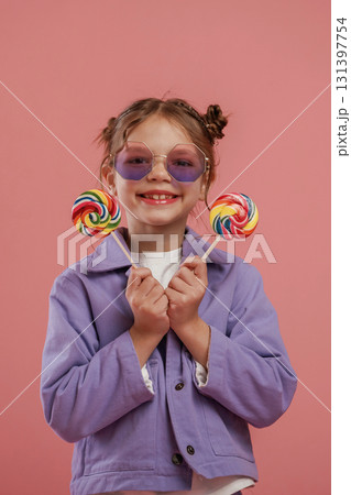 Holding sweet candies. Cute little girl is against pink background Holding sweet candies. Cute little girl is against pink background 131397754