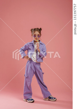 Colorful sweet candy in hand. Cute little girl is against pink background Colorful sweet candy in hand. Cute little girl is against pink background 131397757