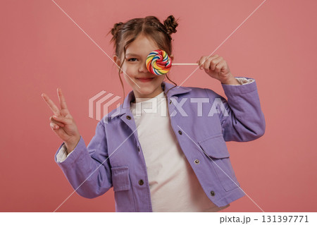Peace hand gesture, with candy. Cute little girl is against pink background 131397771