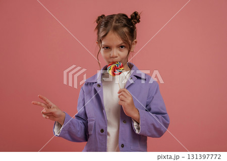 Peace hand gesture, with candy. Cute little girl is against pink background 131397772