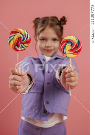 Posing and showing two candies. Cute little girl is against pink background Posing and showing two candies. Cute little girl is against pink background 131397778