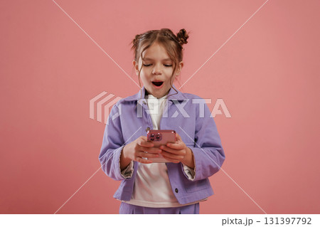 Surprised, using smartphone. Cute little girl is against pink background 131397792