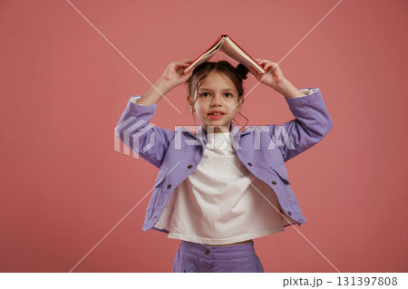 Notepad or book, conception of education. Cute little girl is against pink background Notepad or book, conception of education. Cute little girl is against pink background 131397808