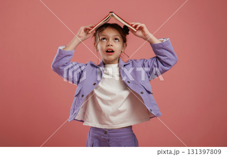 Notepad or book, conception of education. Cute little girl is against pink background Notepad or book, conception of education. Cute little girl is against pink background 131397809