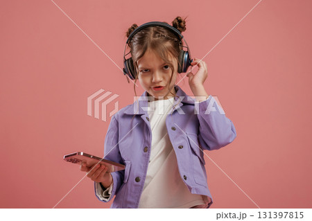 Smartphone and headphones. Cute little girl is against pink background 131397815