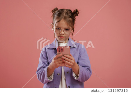Focused by using smartphone. Cute little girl is against pink background 131397816