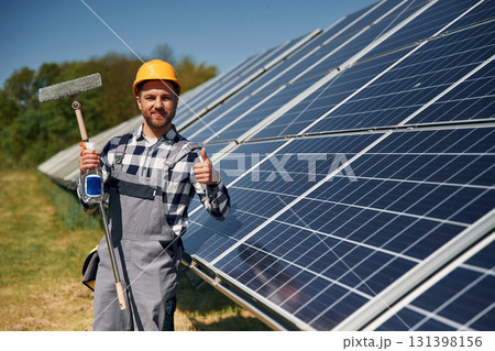 Mop in hands. Cleans the surface. Engineer with photovoltaic solar panels outdoors at daytime 131398156