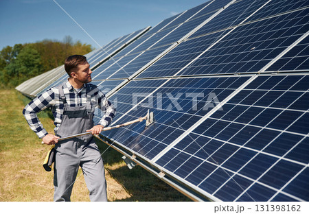 Mop in hands. Cleans the surface. Engineer with photovoltaic solar panels outdoors at daytime Mop in hands. Cleans the surface. Engineer with photovoltaic solar panels outdoors at daytime 131398162
