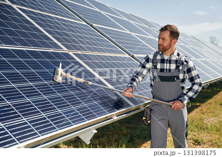 Mop in hands. Cleans the surface. Engineer with photovoltaic solar panels outdoors at daytime Mop in hands. Cleans the surface. Engineer with photovoltaic solar panels outdoors at daytime 131398175