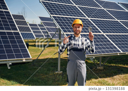 Traditional light bulb in hand. Engineer with photovoltaic solar panels outdoors at daytime Traditional light bulb in hand. Engineer with photovoltaic solar panels outdoors at daytime 131398188
