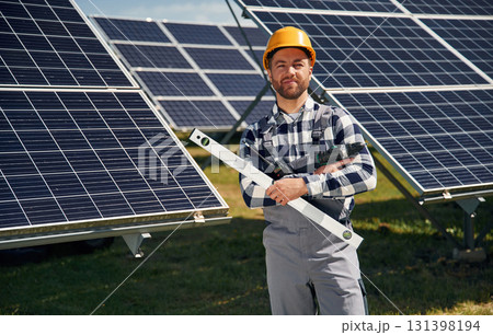Portrait, holding leveler tool. Engineer with photovoltaic solar panels outdoors at daytime Portrait, holding leveler tool. Engineer with photovoltaic solar panels outdoors at daytime 131398194