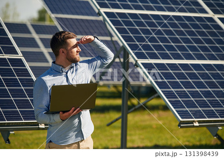 Holding laptop. Engineer with photovoltaic solar panels outdoors at daytime Holding laptop. Engineer with photovoltaic solar panels outdoors at daytime 131398439