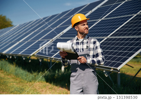 On the field with notepad in hands. Engineer with photovoltaic solar panels outdoors at daytime On the field with notepad in hands. Engineer with photovoltaic solar panels outdoors at daytime 131398530