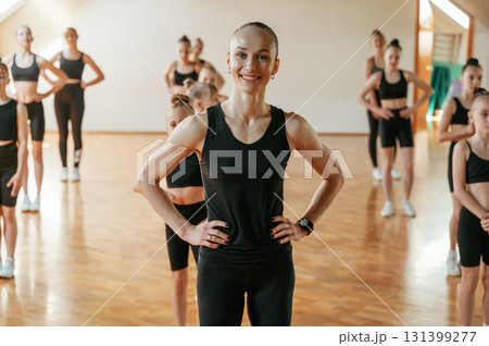 Front view, positive mood. Group of female kids practicing athletic exercises together indoors 131399277